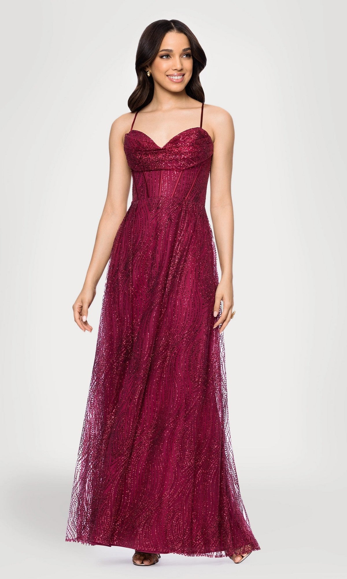 A woman stands against a plain light background wearing the Blondie Nites 5814BN long prom dress in wine, featuring glitter fabric, spaghetti straps, a fitted corset bodice, sleeveless style, and sweetheart neckline.